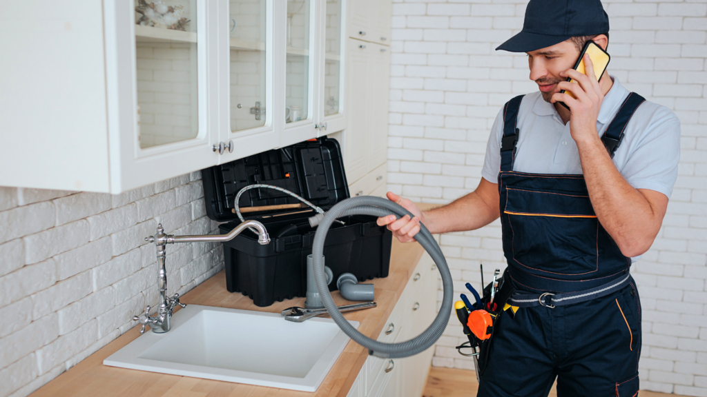 Local service plumber answering phone mid-repair in kitchen