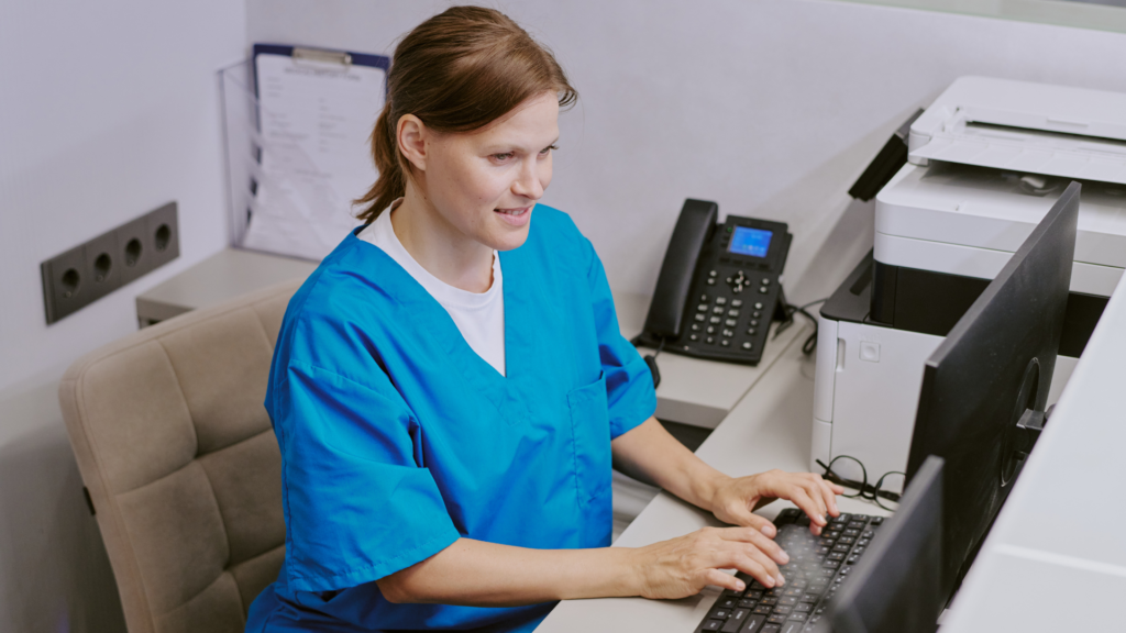 Healthcare worker in scrubs managing patient records on desktop
