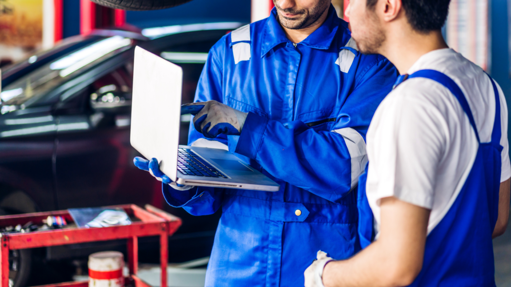 Two mechanics reviewing repair shop website content on laptop