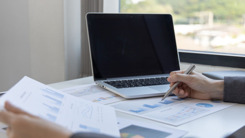 Reviewing customer feedback and performance charts on paper next to a laptop