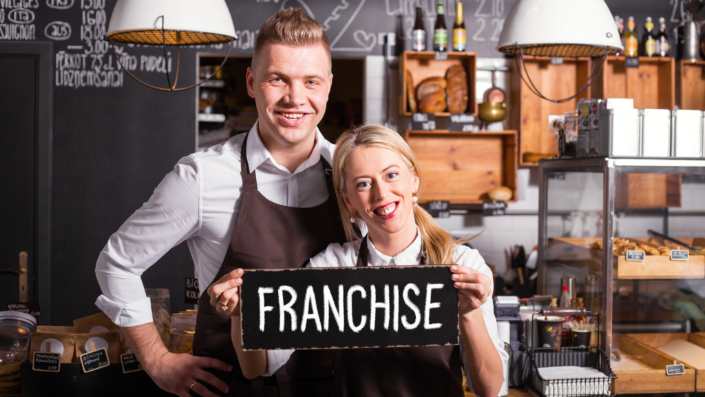 Two franchise owners holding a franchise sign inside their bakery shop